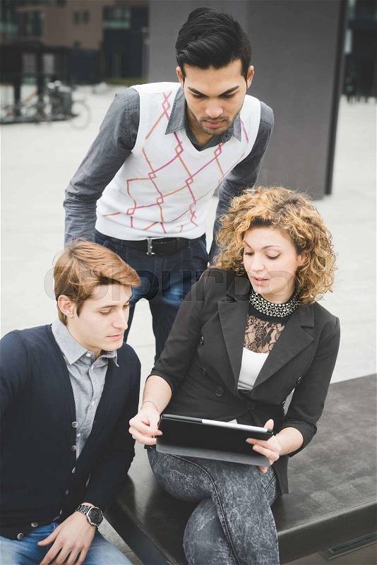 Multiracial contemporary business people working outdoor in town connected with technological devices like laptop, talking to each other watching the screen - business, finance, technology concept, stock photo