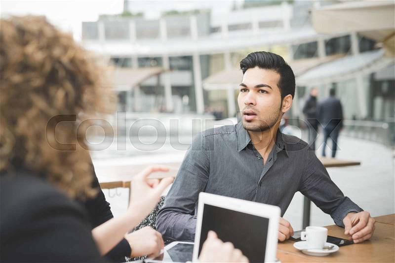 Multiracial contemporary business people working connected with technological devices like tablet and laptop, talking together, sitting in a bar - finance, business, technology concept, stock photo