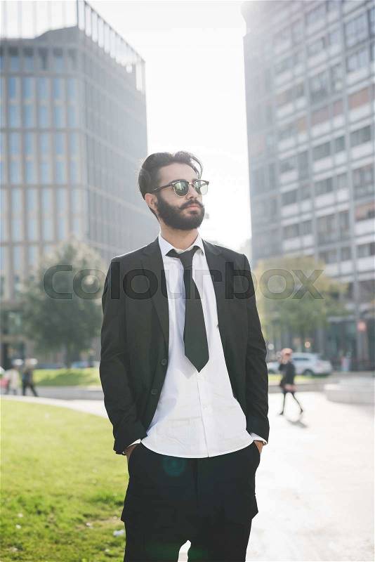 Knee figure of young handsome caucasian black hair modern businessman posing in the city, overlooking left, hands in pocket, serious - working, business, successful concept, stock photo