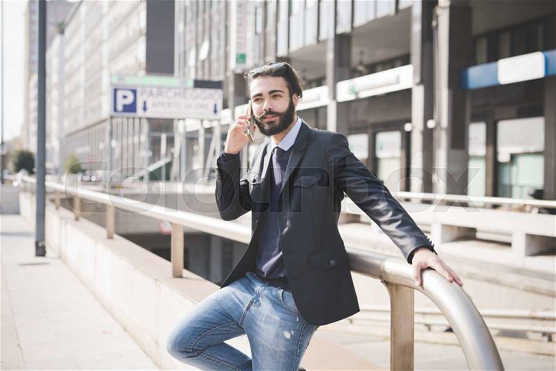 Knee figure of young handsome black hair caucasian modern businessman leaning on a pole in the city backlight, using smartphone - business, working concept, stock photo