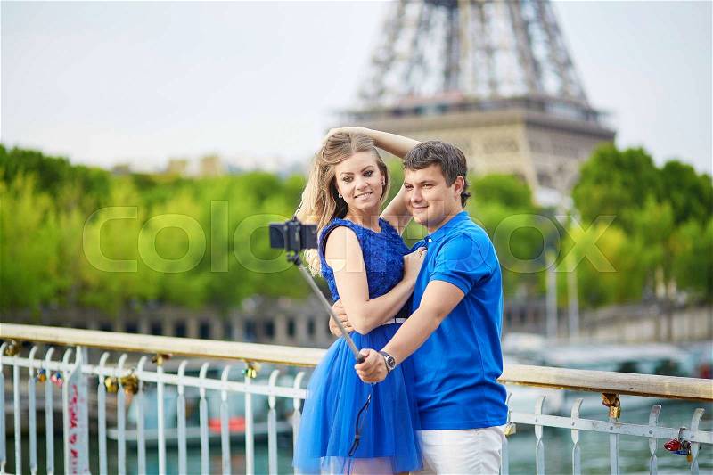 Beautiful young dating couple in Paris making selfie using selfie stick near the Eiffel tower, stock photo