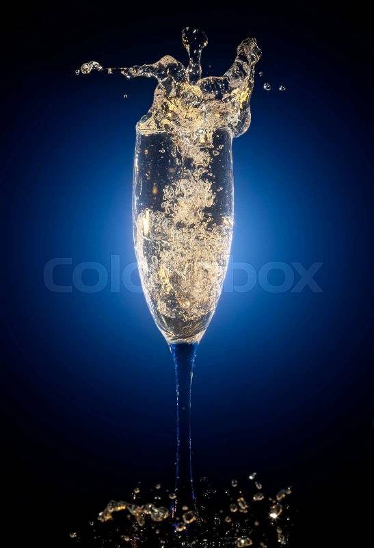 Glass of champagne with splashes and bubbles on blue background, stock photo