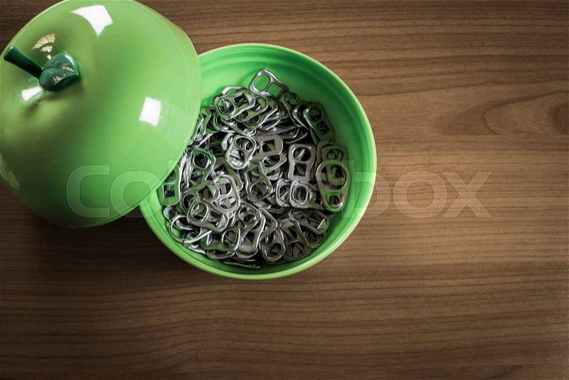 Many metal ring pull in green plastic cup on wooden table, stock photo