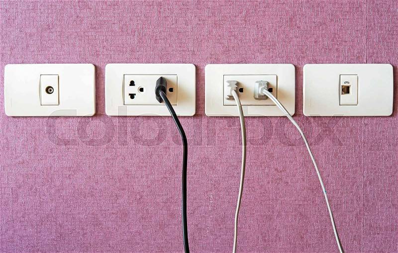 Cables plugged in a white electric outlet mounted on pink wall, stock photo