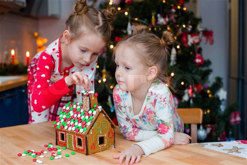 Little adorable girls cooking gingerbread house for Christmas, stock photo