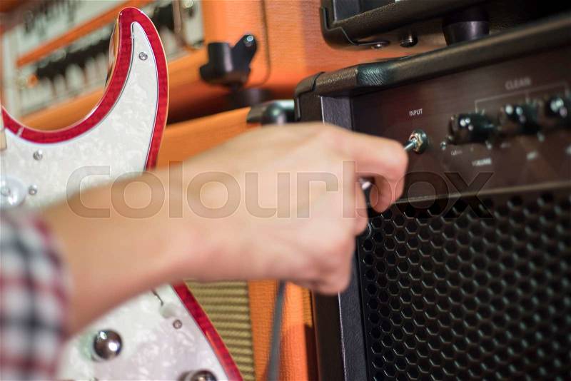 Closed up hand holding jack plug-in to the guitar amplifier, shallow DOF, selected focus, stock photo