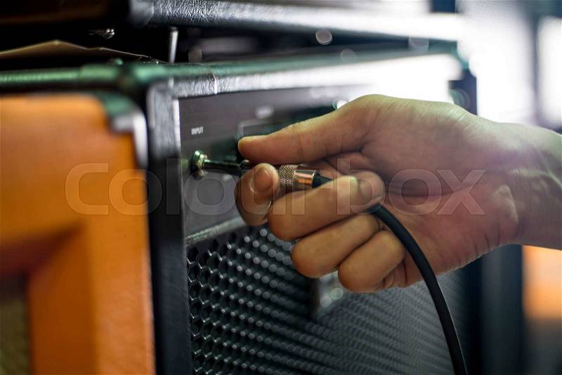 Closed up hand holding jack plug-in to the guitar amplifier, shallow DOF, selected focus, stock photo