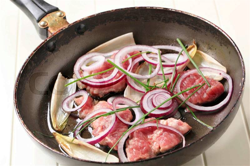 Raw pork, onion, and endive leaves on a frying pan, stock photo
