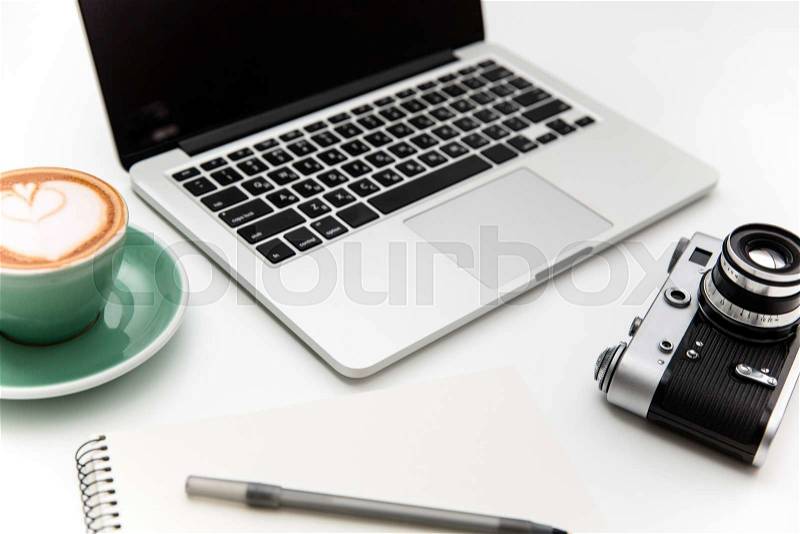 Laptop, vintage camera, cup of coffee, notepad and pen isolated over white background, stock photo