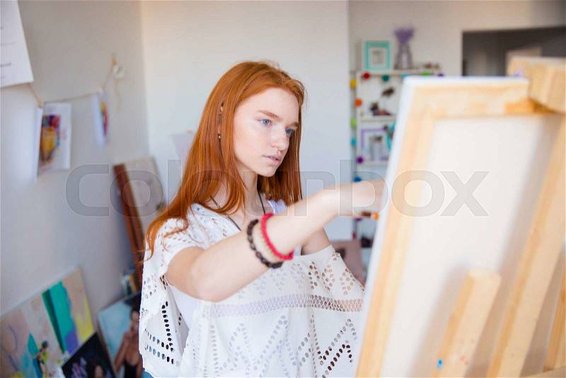 Beautiful pensive young woman painter working in art studio, stock photo