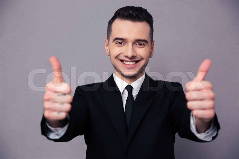 Portrait of a happy businessman showing thumbs up over gray background, stock photo