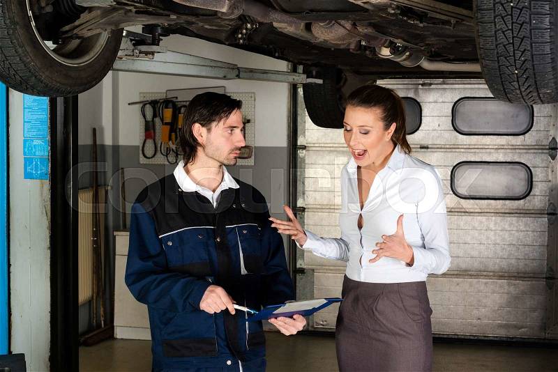 Car mechanic with attractive but angry female customer going through maintenance checklist in garage - apparently the efforts are overpriced since the woman is screaming at the mechanic, stock photo