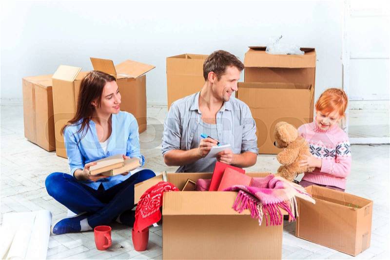 The happy family at repair and relocation. The family sitting and geting things out of boxes against the new white apartment, stock photo