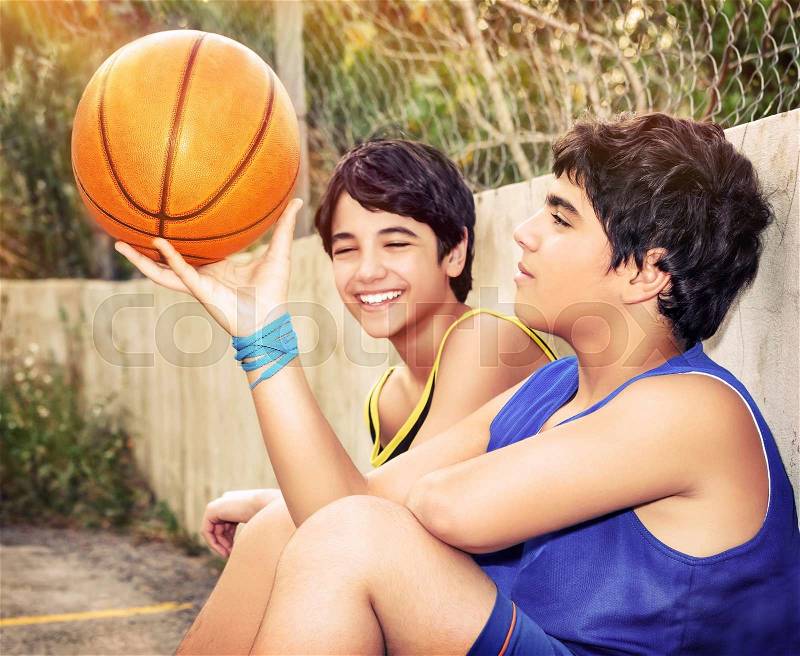 Cute basketball players sitting and resting in timeout, two active teen boys enjoying outdoor games, happy youth lifestyle, stock photo