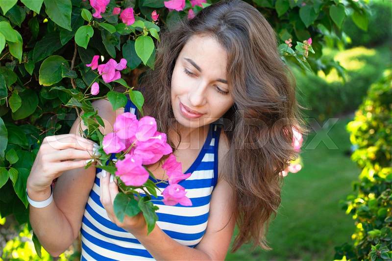 Portrait of young beautiful woman on background of bougainvillea purple violet flowers in blossom, stock photo