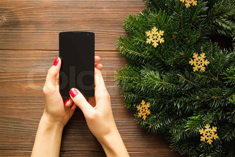 Female hands with red manicure holding a mobile phone with a touch screen on the background of Christmas decorations. View from above, stock photo