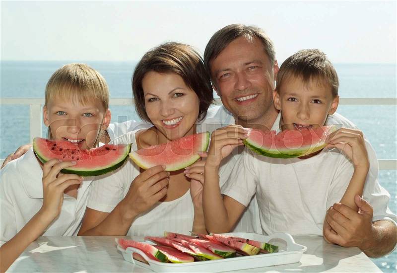 Family eating watermelon in the background of the sea, stock photo