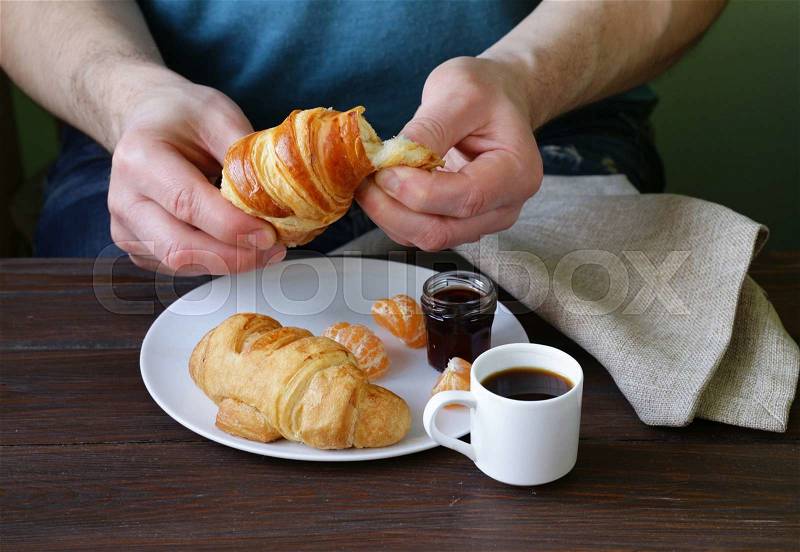 Man eating a croissant with jam for breakfast, stock photo