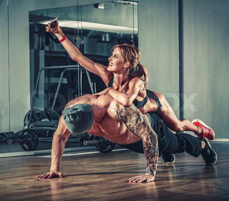 Woman with mobile phone training with muscular handsome man bodybuilder in gym, stock photo