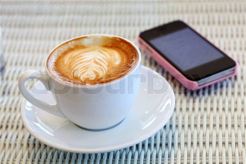 Coffee cup and mobile phone on white table in cafe, stock photo