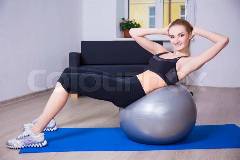 Young beautiful happy woman doing fitness exercises with pilates ball at home, stock photo