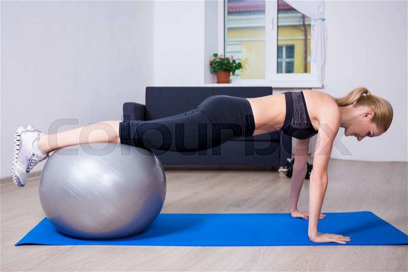 Young beautiful woman doing push up exercise with fit ball at home, stock photo