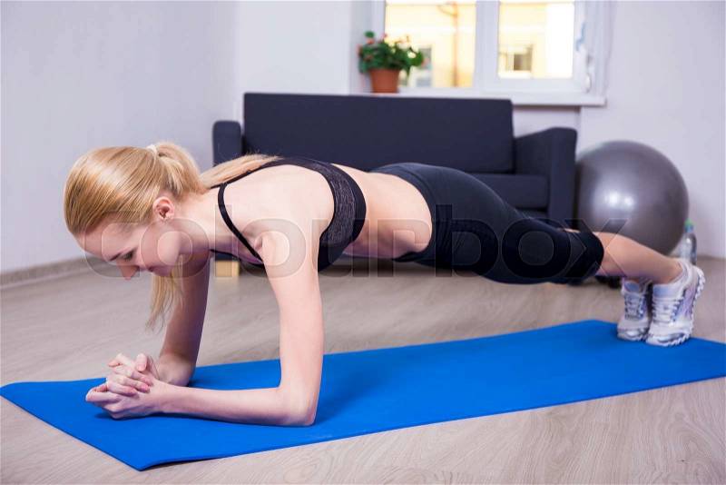 Young sporty slim woman doing plank exercise at home, stock photo