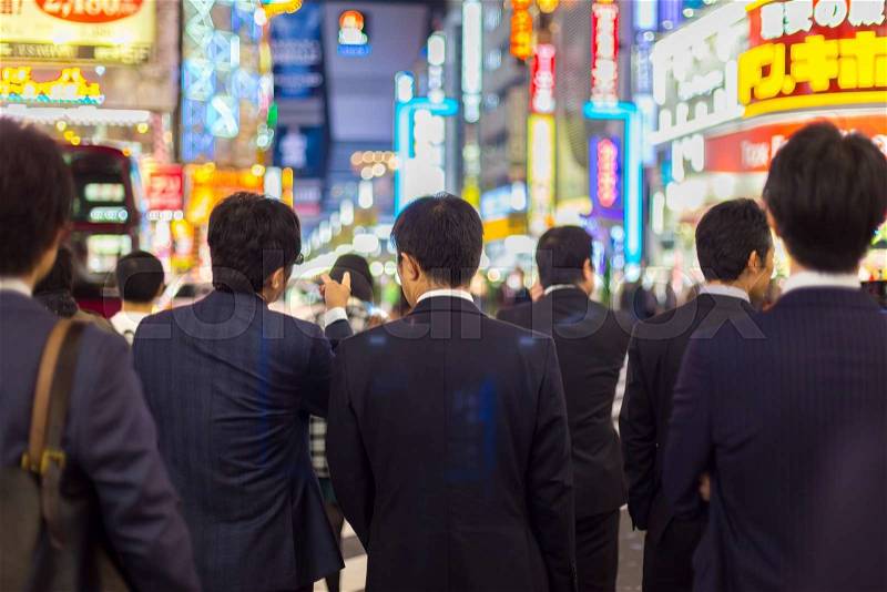 Japanese corporative business people in suits, waiting in rush hour on crossroad in Shinjuku business district, Tokyo, Japan. Blured advertising boards illuminated in the background, stock photo
