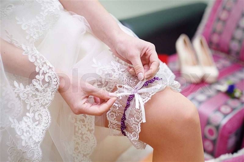 Bride dresses garter on the leg. Picture of beautiful female barefoot legs in wedding dress, stock photo