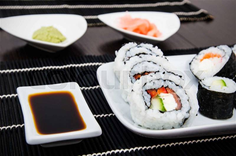 Sushi set on white plate. Black bamboo mat background, stock photo