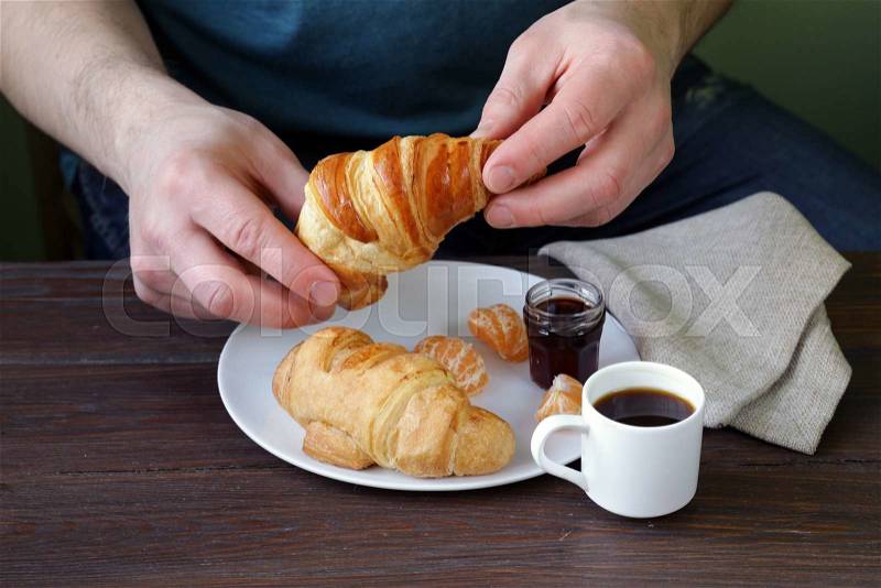Man eating a croissant with jam for breakfast, stock photo