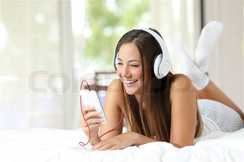 Happy girl listening to the music from a smartphone on the bed at home, stock photo