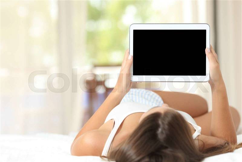 Girl lying on a bed at home using and showing a blank tablet screen, stock photo