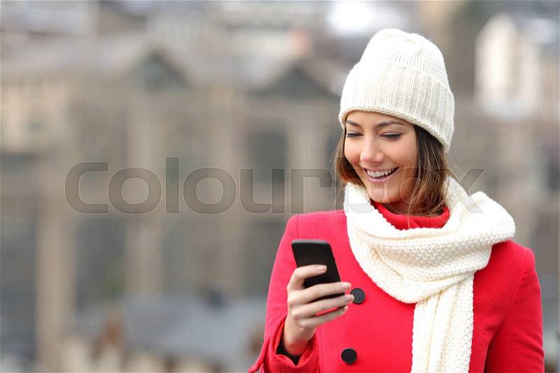 Girl texting in a mobile phone warmly clothed inthe street in winter, stock photo