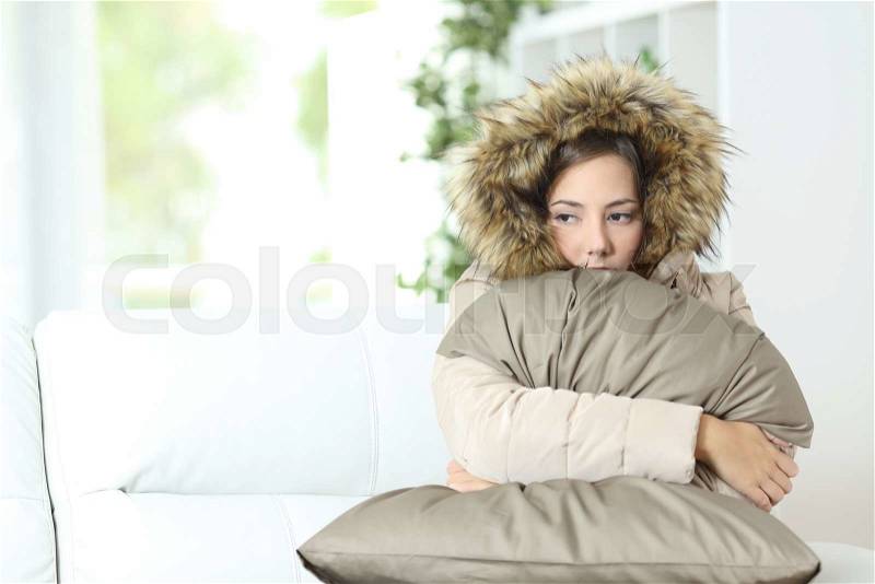 Angry woman warmly clothed in a cold home sitting on a couch, stock photo