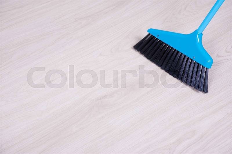Cleaning concept - blue broom sweeping laminated floor, stock photo