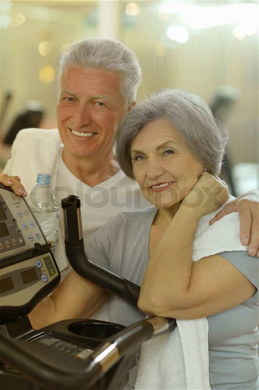 Smiling senior couple drinking water after exercising in gym, stock photo