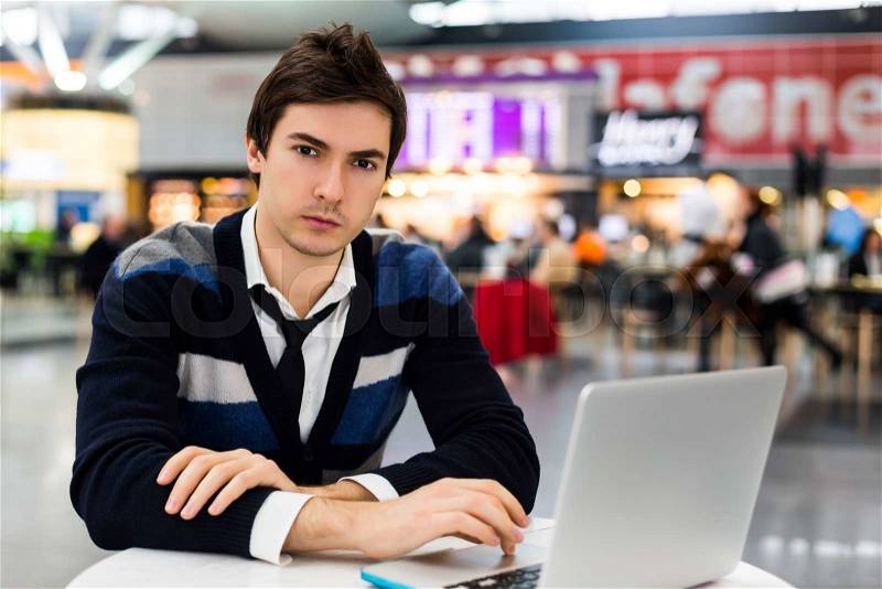 Serious man using modern portable computer on an outdoor table, street on background. Man is freelancer and handsome, stock photo