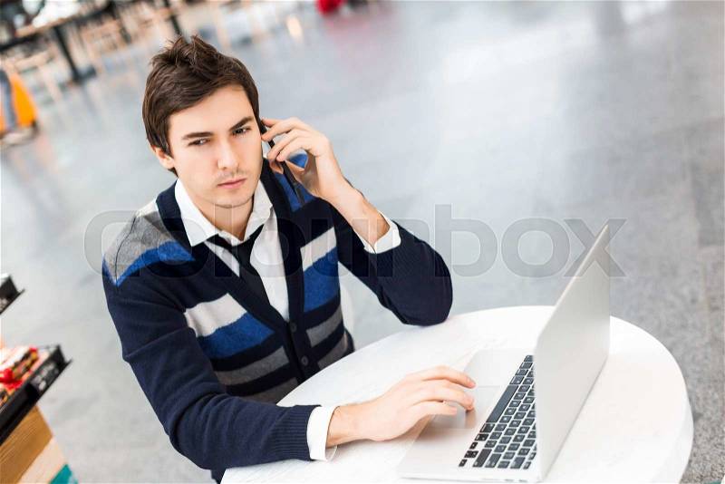 Freelancer work on his computer while talking on smart phone.Male businessman working on notebook in airport, handsome student guy surfing the net outside on terrace out of the office, stock photo