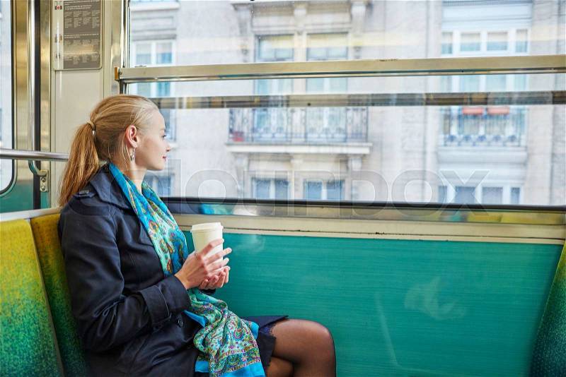 Beautiful young woman travelling in a train of Parisian underground and drinking coffee, stock photo