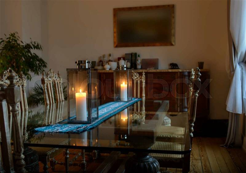 Beautiful interior of a room with a glass table on which there are two burning candles lights dim light from the window, stock photo