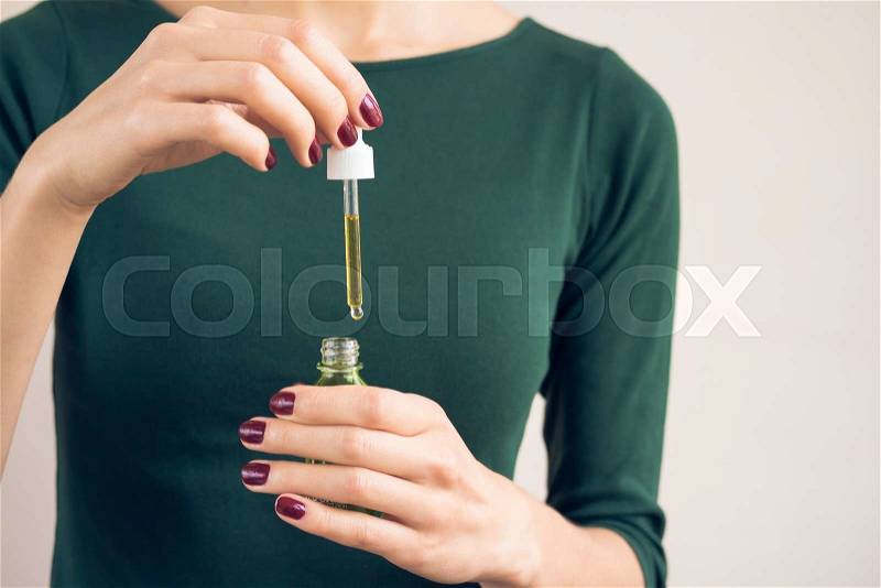 Female hands with a dark red manicure holding cosmetic oil in a bottle with pipette, stock photo