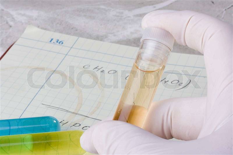 Hand holding a test tube in front of a laboratory notebook, stock photo