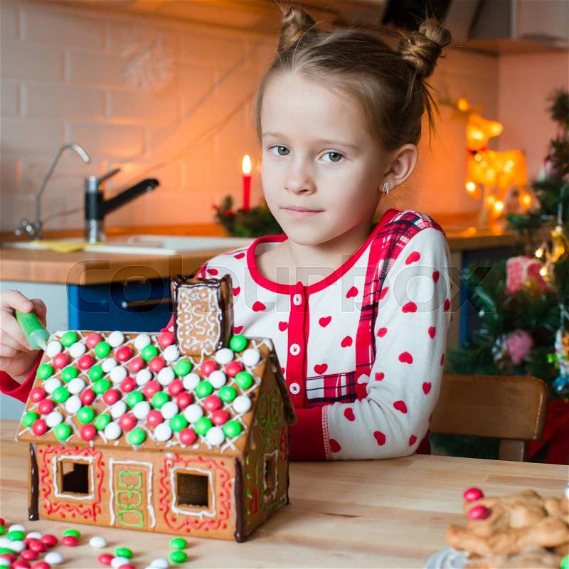 Little adorable girl decorating gingerbread house for Christmas at home, stock photo