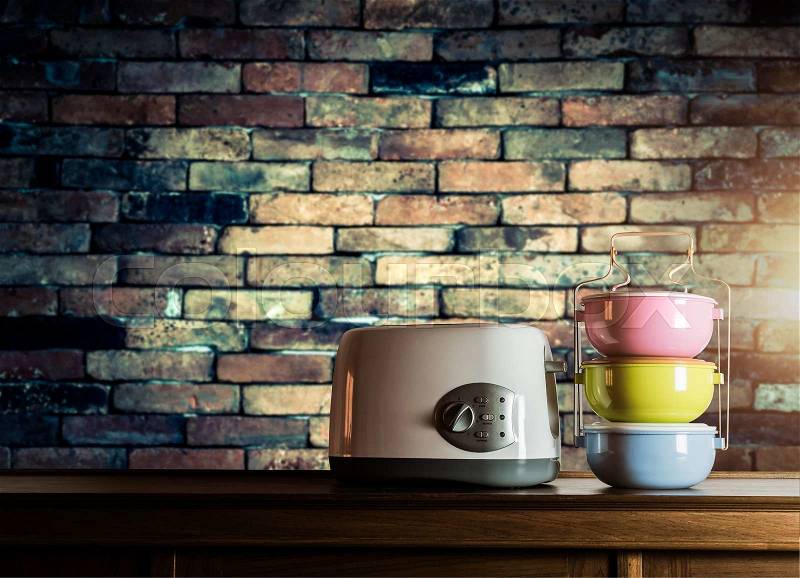 Colorful tiffin carrier and toaster on wooden cupboard with old brick wall background against warm light, stock photo