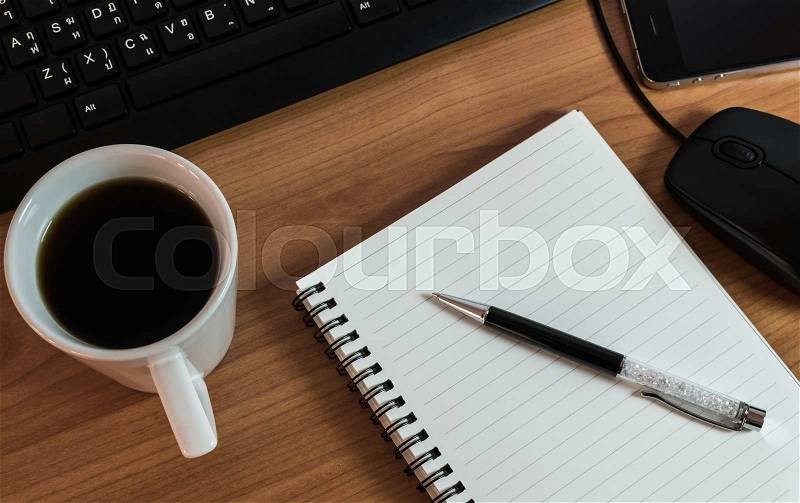 Pen on notebook with coffee computer keyboard, mouse and cell phone on wooden table, stock photo