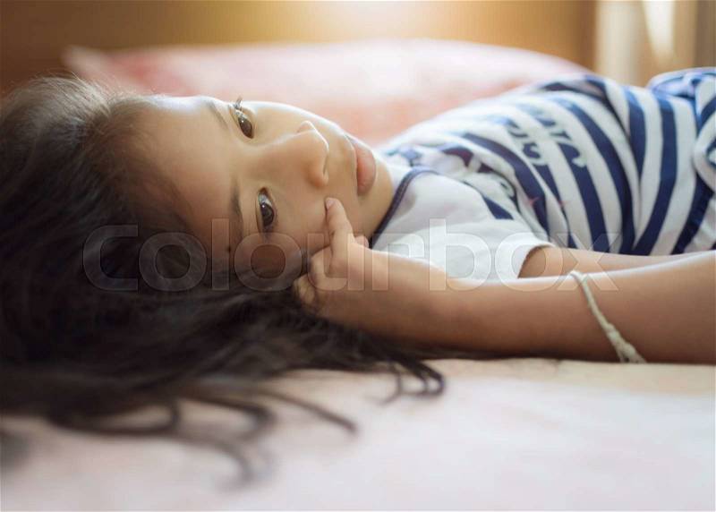 Cute girl lie down on the bed under warm light, stock photo