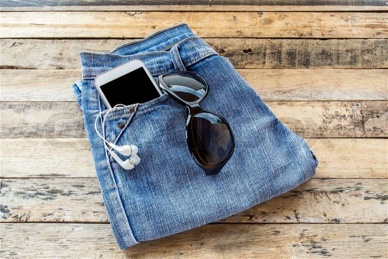 White earphone,sunglasses,smart phone and blue jeans on wooden table background, stock photo