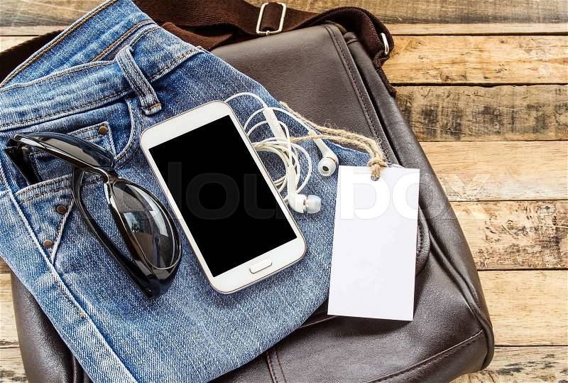 Brown leather bag,blue jean,sunglasses,smart phone and earphone on wooden table background, stock photo