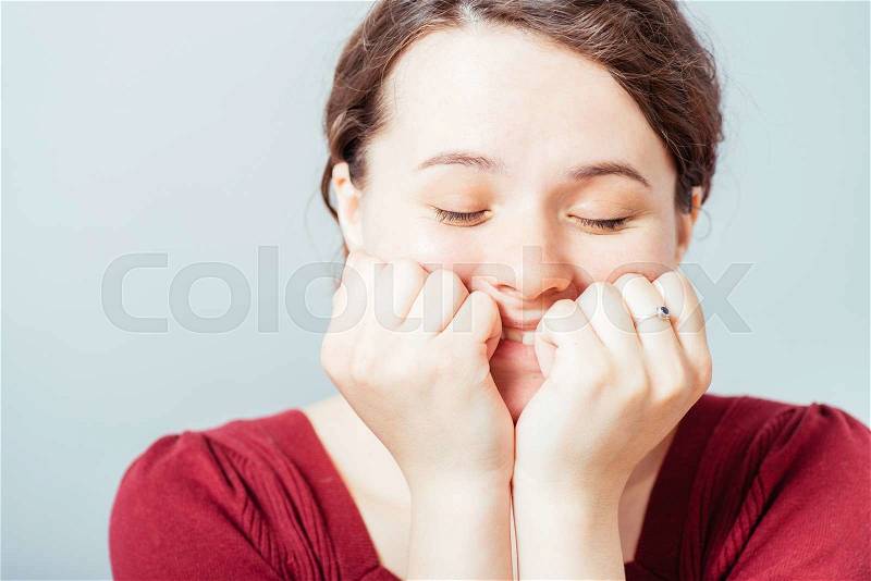 Young woman laughing, hand on face. On a gray background, stock photo
